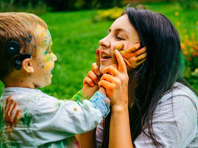 Boy wearing a cochlear implant sound processor laughing with his mother outdoors, a candidate for bimodal hearing aid fitting